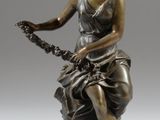 une statue antique en bronze représentant une femme assise sur un rocher