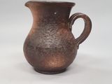 une image représentant un vase marron muni d'une anse, posé sur une surface blanche