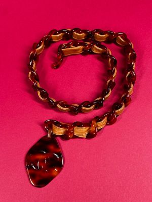 a brown necklace with a brown and black pendant on a pink background