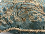 a blue pillow with gold thread on it on a white surface