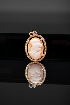un gros plan sur un pendentif plaqué or représentant une femme