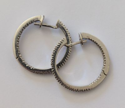 une paire de boucles d'oreilles créoles en argent ornées de petites pointes, sur un fond blanc