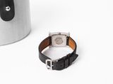 wrist watch with black leather strap next to a silver canister