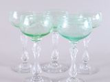 four green wine glasses sitting next to each other on a white surface