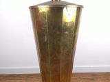 a brass vase sitting on top of a wooden floor next to a white wall