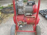a red air compressor sitting on a cart in the dirt