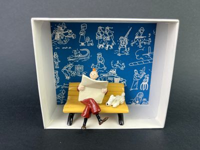 a miniature picture of a person sitting on a bench reading a book