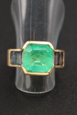 un gros plan d'une bague sertie d'une émeraude verte entourée de saphirs bleus