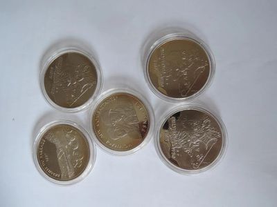 six pièces de monnaie britanniques différentes dans des étuis en plastique, posées sur une surface blanche