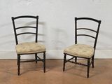 pair of black painted chairs with upholstered seats against a white wall