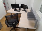a desk with two computers and a chair in the corner