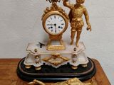 une horloge posée sur une table, surmontée d'une statue