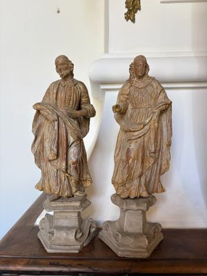 pair of carved statues of two men on pedestals in front of a wall
