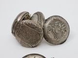 two silver pocket watches and a coin on a white surface