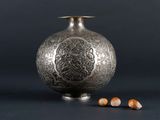 an old silver vase sitting on top of a table next to nuts