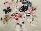 Plusieurs paires de chaussures de bébé sont posées sur un lit recouvert d'une couverture blanche.