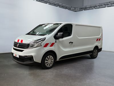 La camionnette blanche est garée dans une grande pièce ; elle porte une bande rouge sur le côté.