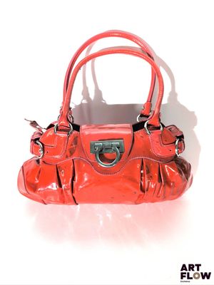 un sac à main rouge posé sur une surface blanche, avec une ombre