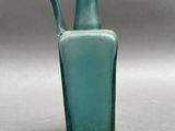 a green glass vase with a handle on a gray surface