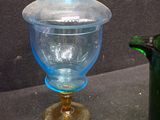 a blue glass jar with a gold lid next to a green glass vase