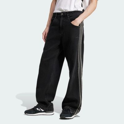 Un homme vêtu d'un pantalon noir et d'un t-shirt blanc se tient debout, les mains dans les poches.