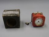 une petite horloge rouge posée à côté d'une petite boîte noire