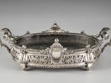 un plat ancien en argent, orné de sculptures raffinées et muni de poignées, posé sur un socle