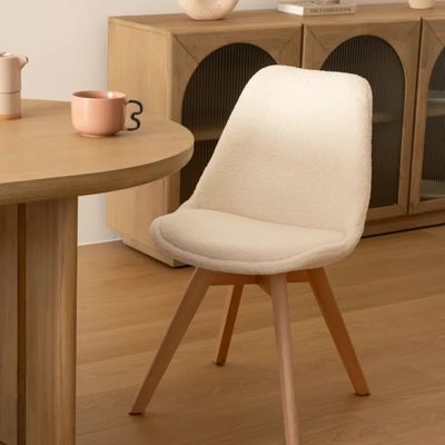 a white chair sitting in front of a table with a vase on it