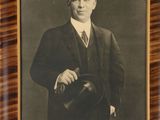 an old photo of a man in a suit and tie holding a hat