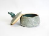a small green pot with a lid on a white surface