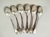 six silver spoons are lined up on a white surface