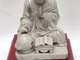 statue of a monk sitting on a red platform with a book and a ball