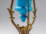 a gold and blue vase on a stand on a white background