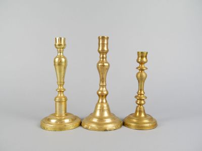 trois bougeoirs dorés posés sur une surface blanche