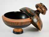 a black and orange bowl with a lid sitting on a stand