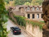 a car that is driving down the road by a stone wall