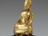 une image représentant une statue en or d'une personne assise sur un socle noir