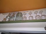 bottles and glasses are lined up on a shelf in a kitchen