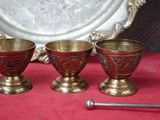 quatre tasses en laiton vieilli et une cuillère posées sur une nappe rouge