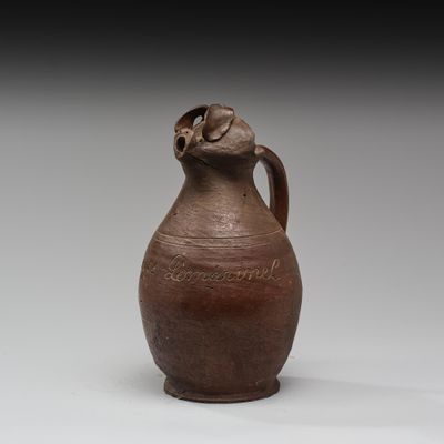 un vieux vase marron posé sur une table près d'un mur blanc