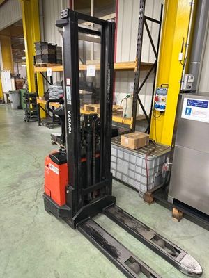 un chariot élévateur garé dans un entrepôt, avec des cartons posés au sol