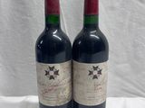 two bottles of red wine sitting on top of a white table