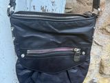 un sac à main noir muni de fermetures éclair, suspendu à un poteau en bois près d'un mur en pierre