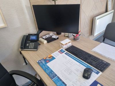 un bureau sur lequel se trouvent un ordinateur, un clavier, un téléphone et d'autres objets