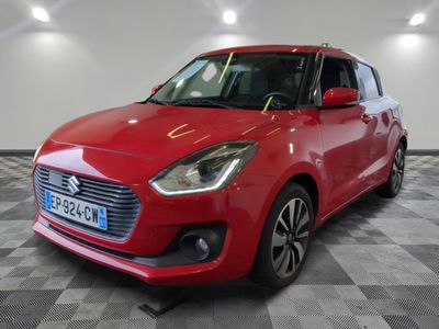 Une Suzuki Swift rouge est garée dans une pièce au sol à carreaux.
