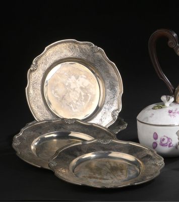 trois assiettes en argent et une théière en argent posées sur une table noire