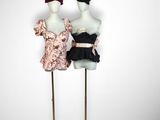 two mannequins dressed in black and pink dresses stand on a gold stand