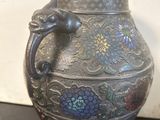 un vase en argent orné d'une poignée en forme de dragon, posé sur une table