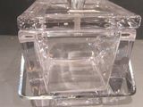 une boîte en verre transparent avec un couvercle argenté, posée sur une table
