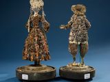two figurines of women in dresses and hats on pedestals